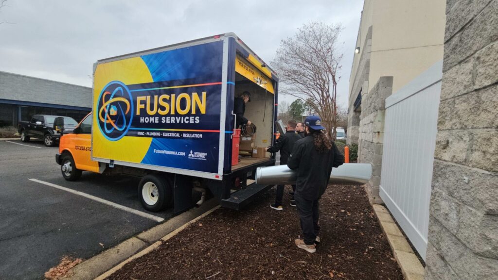 Technicians loading insulation into Fusion HVAC service truck in parking lot.